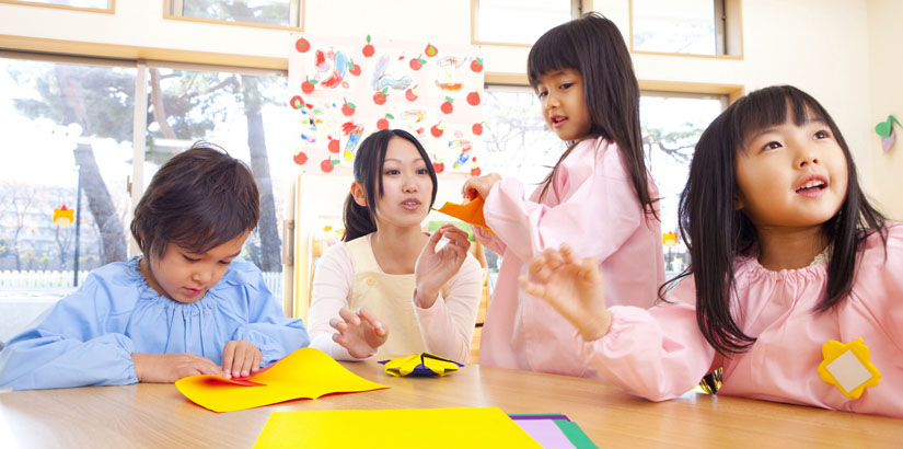 Kindergarten children and teacher fold origami